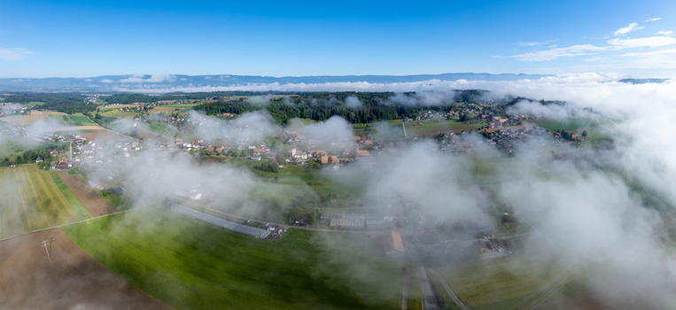 Aerial view of the village of Grossaffoltern partially covered by morning mist and low clouds with green fields and distant mountains Grossaffoltern Canton of Bern Switzerland. Aerial view of the village of Grossaffoltern partially covered by morning mist and low clouds with green fields and distant mountains Grossaffoltern Canton of Bern Switzerland.