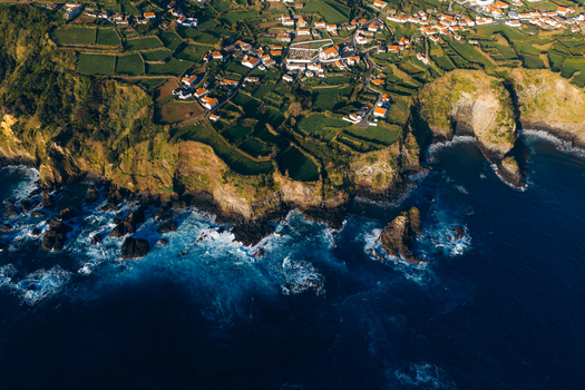 Aerial view of a coastal village with green agricultural fields and rugged volcanic cliffs overlooking the blue Atlantic Ocean in Ponta Delgada Acores Portugal. Aerial view of a coastal village with green agricultural fields and rugged volcanic cliffs overlooking the blue Atlantic Ocean in Ponta Delgada Acores Portugal.