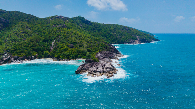 Aerial view of the lush green coastline and rocky headland of Anse Soleil Beachcomber Hotel surrounded by turquoise ocean waters in Mahe Baie Lazare Seychelles.