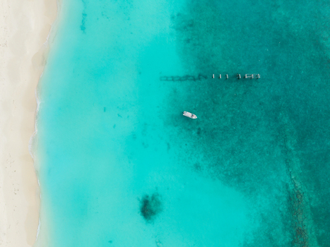 Aerial view of a solitary boat gently floating over the turquoise waters near a weathered pier contrasting with the white sandy beach Hoarafushi Maldives. Aerial view of a solitary boat gently floating over the turquoise waters near a weathered pier contrasting with the white sandy beach Hoarafushi Maldives.