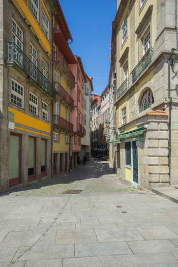 Porto Portugal 13 July 2021 View of the narrow sun drenched street framed by historic buildings with vibrant facades under a clear blue sky creating a captivating urban scene. Porto Portugal 13 July 2021 View of the narrow sun drenched street framed by historic buildings with vibrant facades under a clear blue sky creating a captivating urban scene.