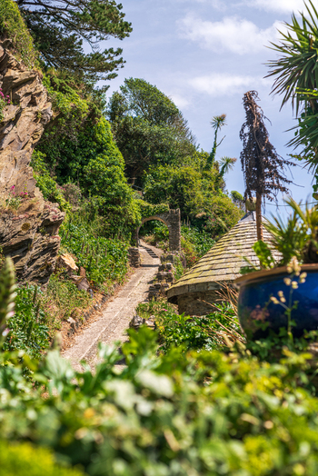 View of a stone pathway winding through lush coastal vegetation and a historic stone archway in the village of Polperro Cornwall United Kingdom. View of a stone pathway winding through lush coastal vegetation and a historic stone archway in the village of Polperro Cornwall United Kingdom.
