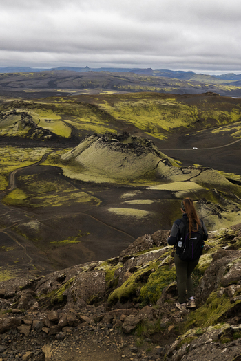 View of a hiker descending a rocky slope overlooking a dramatic volcanic landscape with moss covered hills under a cloudy sky Skaftárhreppur Iceland. View of a hiker descending a rocky slope overlooking a dramatic volcanic landscape with moss covered hills under a cloudy sky Skaftárhreppur Iceland.