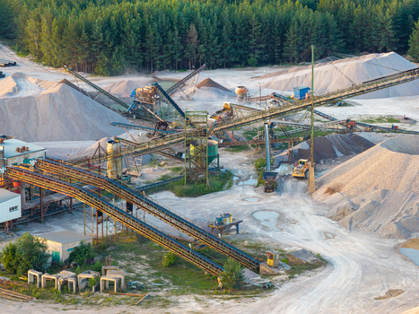 Aerial view of a large scale sand and gravel mine featuring extensive conveyor belt systems piles of processed aggregate heavy machinery and surrounding forest in Poland.