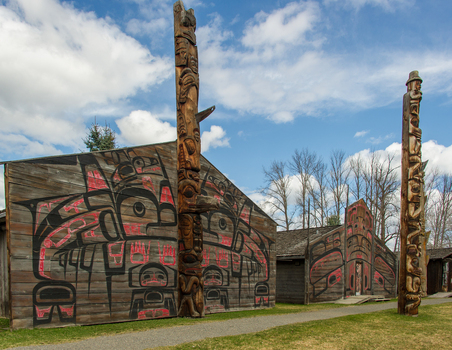 View of Ksan Historical Village featuring traditional totem poles and longhouses with intricate indigenous art under a blue sky in Ksan British Columbia Canada. View of Ksan Historical Village featuring traditional totem poles and longhouses with intricate indigenous art under a blue sky in Ksan British Columbia Canada.