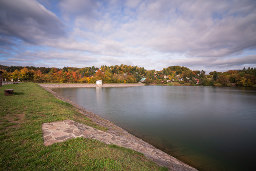 View of Velka Richnava lake with autumn foliage on the surrounding hills and a stone embankment in Stiavnicke Bane Banska Bystrica Regio Slovakia.