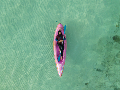 Aerial view of a woman in a pink kayak with a blue paddle floats on the turquoise water near Menjangan Kecil Island Karimunjawa Indonesia.