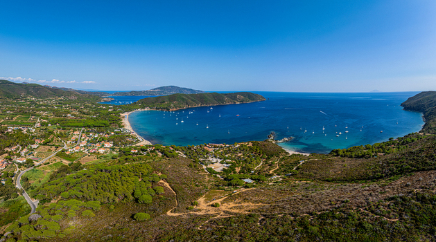 Aerial view of Lacona Beach with turquoise waters anchored boats and lush Mediterranean vegetation along the coastline in Lacona Tuscany Italy.