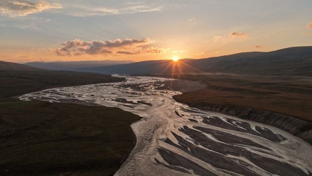 Aerial view of the Enilchek River winding through the rugged landscape at sunset with golden light reflecting on the water. Enilchek Issyk Kul Region Kyrgyzstan. Aerial view of the Enilchek River winding through the rugged landscape at sunset with golden light reflecting on the water. Enilchek Issyk Kul Region Kyrgyzstan.