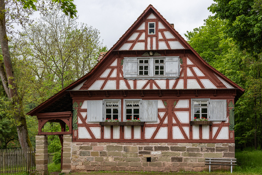 View of a traditional half timbered house at the Hennebergisches Museum Kloster Vessra with red timbering and grey shutters surrounded by green trees in Kloster Vessra Thuringen Germany.