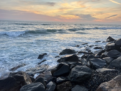 View of ocean waves crashing against dark rocks on the shoreline under a sunset sky in Oceanside California United States. View of ocean waves crashing against dark rocks on the shoreline under a sunset sky in Oceanside California United States.