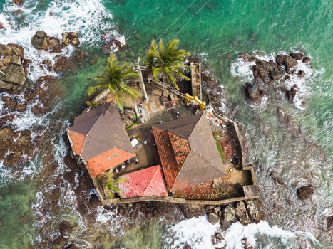 Aerial view of Seenigama Muhudu Dewalaya temple on a rocky island surrounded by turquoise ocean waves and palm trees in Peraliya Sri Lanka. Aerial view of Seenigama Muhudu Dewalaya temple on a rocky island surrounded by turquoise ocean waves and palm trees in Peraliya Sri Lanka.