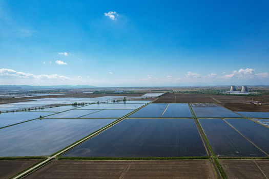 Aerial view of flooded rice fields reflecting the blue sky with cooling towers of a power plant on the horizon in Trino Piemonte Italy.