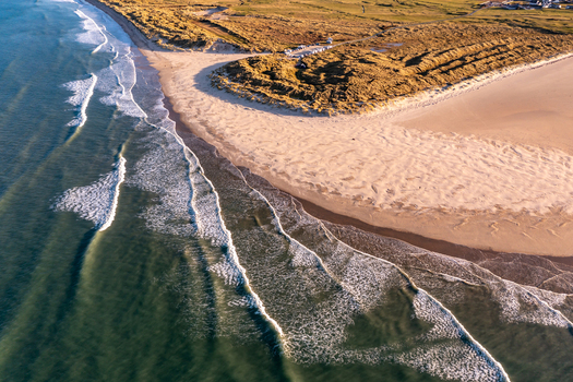 Aerial view of Sheephaven Bay featuring golden sandy beaches rolling waves and grassy dunes under warm sunlight in Dunfanaghy County Donegal Ireland. Aerial view of Sheephaven Bay featuring golden sandy beaches rolling waves and grassy dunes under warm sunlight in Dunfanaghy County Donegal Ireland.