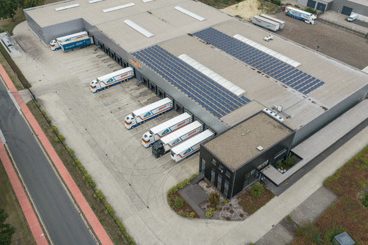 Genk Belgium 27 August 2026 Aerial view of a logistics distribution center with multiple freight trucks at loading docks and solar panels installed on the warehouse roof.