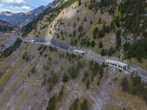 Aerial view of the Albanian Alps featuring a winding mountain road with concrete tunnels carved into the steep rocky slopes with pine trees in Shkoder Shkoder County Albania. Aerial view of the Albanian Alps featuring a winding mountain road with concrete tunnels carved into the steep rocky slopes with pine trees in Shkoder Shkoder County Albania.