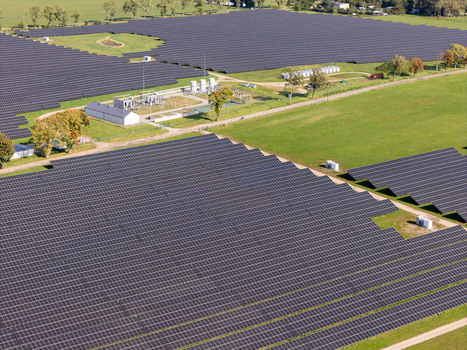 Aerial view of a large solar farm with rows of photovoltaic panels green grassy fields and an electrical substation in Poland.