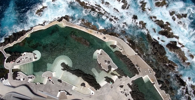 Aerial view of the Porto Moniz Natural Swimming Pools featuring volcanic rock formations and clear seawater surrounded by crashing waves in Porto Moniz Madeira Portugal. Aerial view of the Porto Moniz Natural Swimming Pools featuring volcanic rock formations and clear seawater surrounded by crashing waves in Porto Moniz Madeira Portugal.