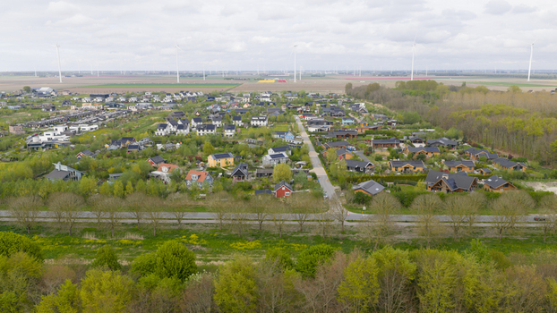 Aerial view of Ecodorp Bolderburen featuring sustainable houses with solar panels surrounded by lush greenery and wind turbines in Almere Flevoland Netherlands. Aerial view of Ecodorp Bolderburen featuring sustainable houses with solar panels surrounded by lush greenery and wind turbines in Almere Flevoland Netherlands.