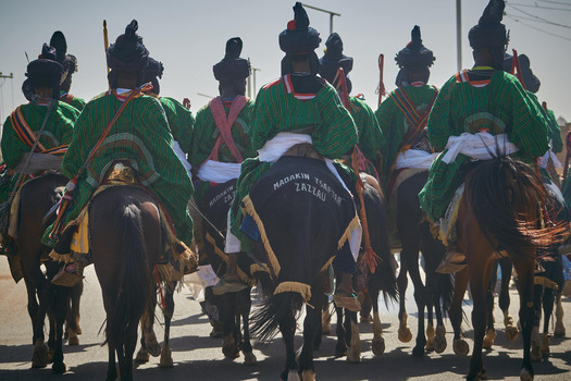 Zaria city Nigeria 21 March 2026 View of a vibrant procession of horsemen in traditional green and black regalia their dark steeds kicking up dust under the bright sun. Zaria city Nigeria 21 March 2026 View of a vibrant procession of horsemen in traditional green and black regalia their dark steeds kicking up dust under the bright sun.