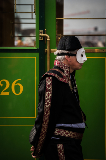 Basel Switzerland 10 March 2025 View of a masked figure in traditional attire stands poised against the vibrant green of a passing tram evoking the festive spirit of Fasnacht.. Basel Switzerland 10 March 2025 View of a masked figure in traditional attire stands poised against the vibrant green of a passing tram evoking the festive spirit of Fasnacht..