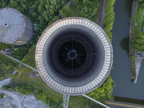 Aerial view of the massive circular cooling tower of the abandoned IM power plant surrounded by lush green trees a river and industrial structures in Charleroi Wallonia Belgium.
