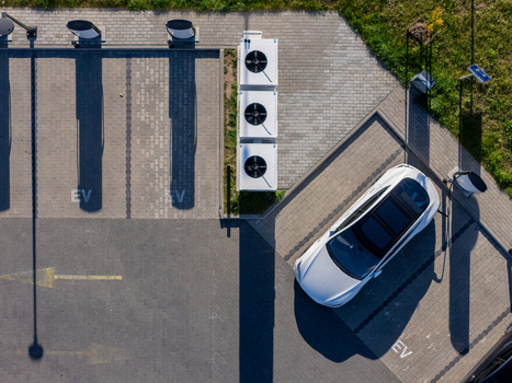 Aerial view of an electric vehicle charging station with a white car parked and charging featuring paved parking spaces and HVAC units in Gdansk Poland. Aerial view of an electric vehicle charging station with a white car parked and charging featuring paved parking spaces and HVAC units in Gdansk Poland.