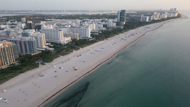 Aerial view of the coastline of Miami Beach with high rise hotels and condominiums lining the sandy shore turquoise ocean waters and clear sky in Miami Beach Florida United States. Aerial view of the coastline of Miami Beach with high rise hotels and condominiums lining the sandy shore turquoise ocean waters and clear sky in Miami Beach Florida United States.