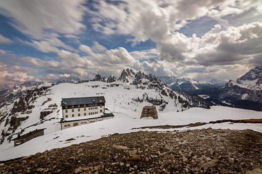 View of a mountain hut nestled among the snow covered peaks of the Dolomites under a dramatic cloudy sky in Trentino Alto Adige Italy. View of a mountain hut nestled among the snow covered peaks of the Dolomites under a dramatic cloudy sky in Trentino Alto Adige Italy.