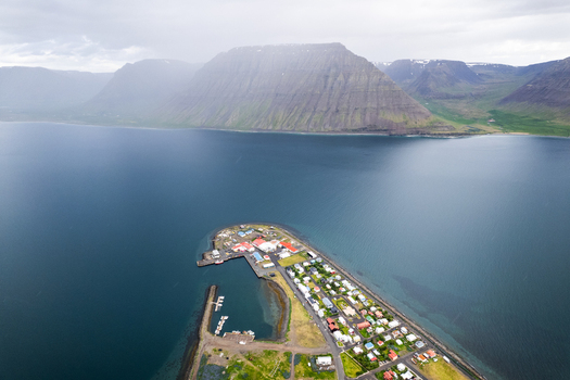 Aerial view of the coastal village of Flateyri situated on a narrow spit of land surrounded by calm fjord waters and massive table mountains under a misty sky in Flateyri Isafjardarbaer Iceland.