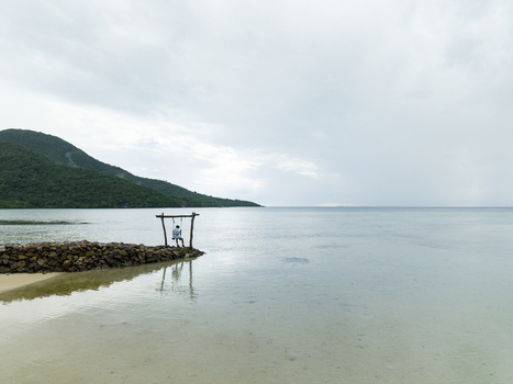 Aerial view of a lone figure standing by a rustic wooden structure on Bobby Beach where the tranquil sea meets the shore Karimunjawa Jawa Tengah Indonesia.