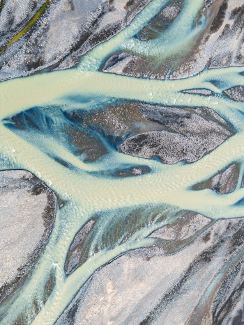 Aerial view of a braided glacial river with milky blue meltwater flowing through dark volcanic gravel beds in Iceland. Aerial view of a braided glacial river with milky blue meltwater flowing through dark volcanic gravel beds in Iceland.