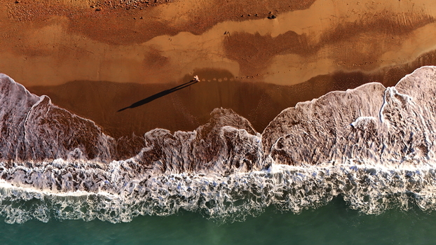 Aerial view of Manavgat Mendirek with waves crashing onto the sandy beach and a long shadow cast on the shore in Manavgat Antalya Turkiye.