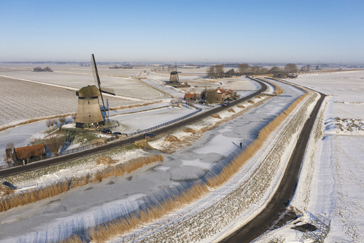 Aerial view of traditional Dutch windmills situated along a frozen canal in a snow covered rural landscape in Ursem North Holland Netherlands.
