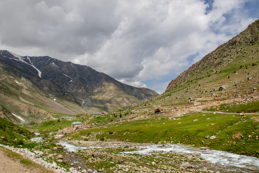 View of Astore Valley featuring a flowing river lush green mountain slopes and distant snow capped peaks under a cloudy sky Astore Gilgit Pakistan. View of Astore Valley featuring a flowing river lush green mountain slopes and distant snow capped peaks under a cloudy sky Astore Gilgit Pakistan.