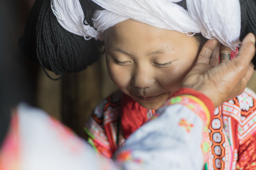 Gaoxing China 29 April 2026 View of a young Long Horn Miao girl in traditional dress with a large wool headpiece being adjusted by an elder. Gaoxing China 29 April 2026 View of a young Long Horn Miao girl in traditional dress with a large wool headpiece being adjusted by an elder.