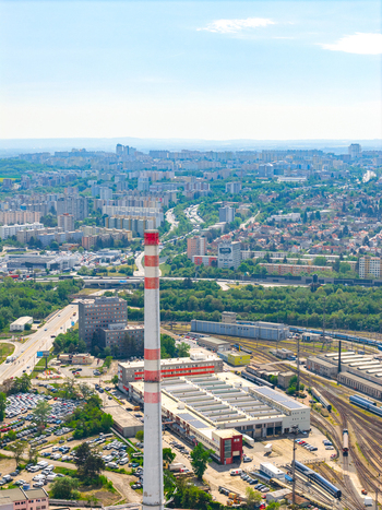 Aerial view of a tall red and white striped industrial chimney rising above a complex with railway tracks a parking lot and the sprawling city skyline in Prague Prague Czechia.