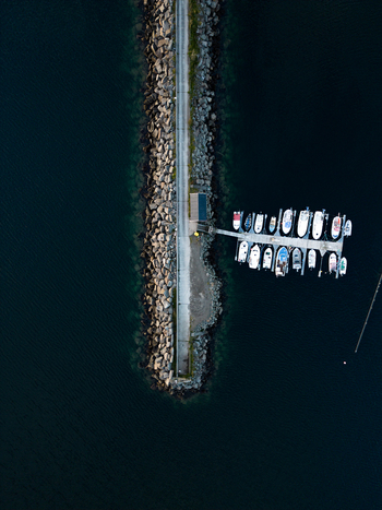 Aerial view of the Tangstad breakwater and floating dock with moored boats in the dark blue waters of Leknes Nordland Norway. Aerial view of the Tangstad breakwater and floating dock with moored boats in the dark blue waters of Leknes Nordland Norway.