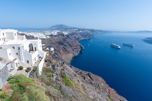 View of the iconic white buildings of Fira perched on the volcanic cliffs overlooking the caldera and the deep blue Aegean Sea with cruise ships in Fira Greece. View of the iconic white buildings of Fira perched on the volcanic cliffs overlooking the caldera and the deep blue Aegean Sea with cruise ships in Fira Greece.
