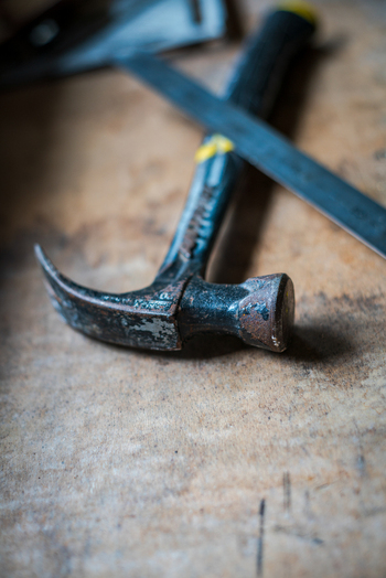 View of a metal hammer and a ruler resting on a worn wooden workbench in Looe Cornwall United Kingdom. View of a metal hammer and a ruler resting on a worn wooden workbench in Looe Cornwall United Kingdom.
