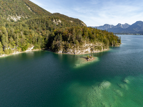 Aerial view of the Ochsenkreuz cross on a small islet in the turquoise waters of a lake surrounded by forested hills and mountains in Salzburg Umgebung Salzburg Austria.