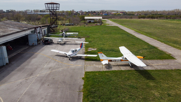 Serbia 11 April 2021 Aerial view of a small airfield with light aircraft parked on the tarmac and grass featuring a hangar and a control tower under a clear sky. Serbia 11 April 2021 Aerial view of a small airfield with light aircraft parked on the tarmac and grass featuring a hangar and a control tower under a clear sky.