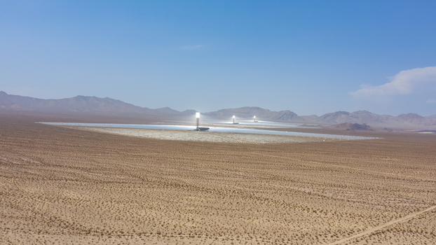 Aerial view of a large concentrated solar power plant with thousands of mirrors and central solar towers situated in a vast desert landscape in the United States.