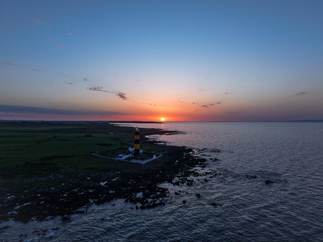 Aerial view of St John s Point Lighthouse at sunset with rocky coastline green fields and calm sea in Newcastle Northern Ireland United Kingdom. Aerial view of St John s Point Lighthouse at sunset with rocky coastline green fields and calm sea in Newcastle Northern Ireland United Kingdom.