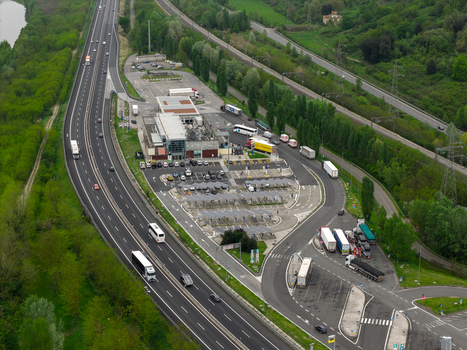 Aerial view of a highway service station with parked trucks and cars traveling along the motorway surrounded by green trees in San Giovanni Valdarno Tuscany Italy.