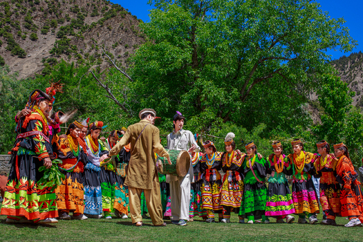 Chitral Khyber Pakhtunkhwa Pakistan 15 May 2013 View of Kalash people in traditional colorful clothing performing a dance in Rumbur Valley with mountains in the background.