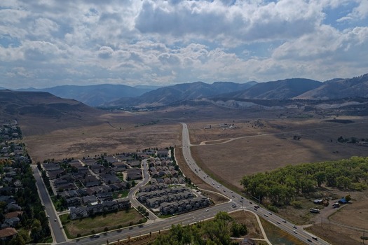 Aerial view of a suburban neighborhood with residential homes a winding road and expansive open fields set against the backdrop of the Rocky Mountains in Golden Colorado United States.