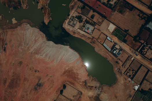 Aerial view of a green pond reflecting the sun near the Kano Madobi Kiru Road with surrounding buildings and red arid soil in Watari Kano Nigeria. Aerial view of a green pond reflecting the sun near the Kano Madobi Kiru Road with surrounding buildings and red arid soil in Watari Kano Nigeria.