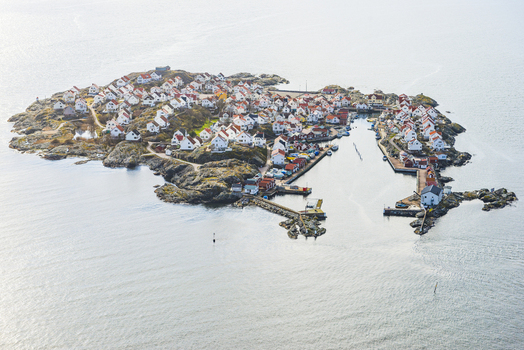 Aerial view of the island of Astol with its dense cluster of white houses rocky coastline and small harbor filled with boats in Astol Vastra Gotaland County Sweden.