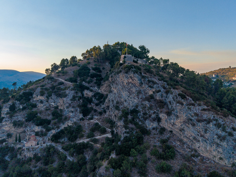 Aerial view of the historic Berat Castle perched on a rocky hill surrounded by lush trees and rugged terrain under a clear sky in Berat Berat County Albania.